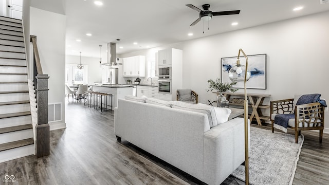 living area with dark wood-style floors, ceiling fan with notable chandelier, stairs, and recessed lighting