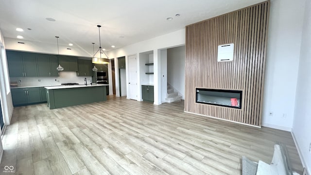 kitchen with sink, a center island with sink, decorative light fixtures, and light wood-type flooring