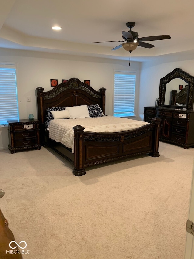 carpeted bedroom with ceiling fan and a tray ceiling