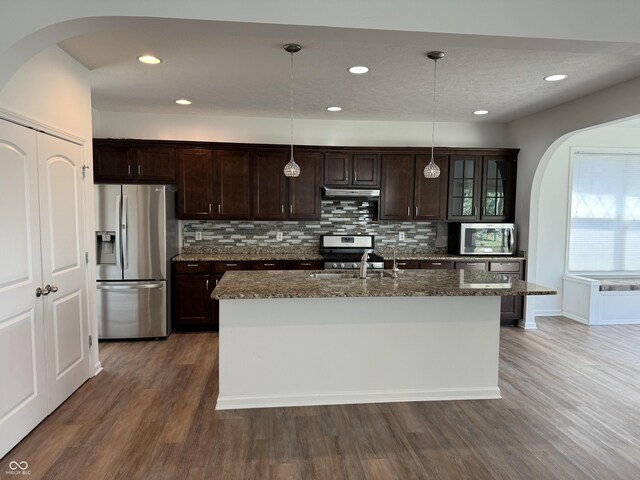 kitchen with sink, dark brown cabinets, hanging light fixtures, a center island with sink, and stainless steel appliances