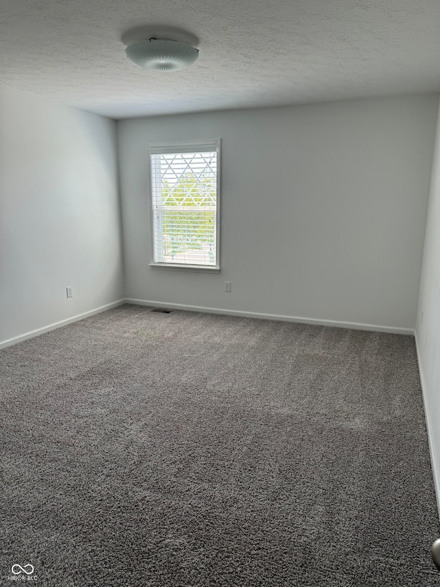 unfurnished room with a textured ceiling and dark colored carpet