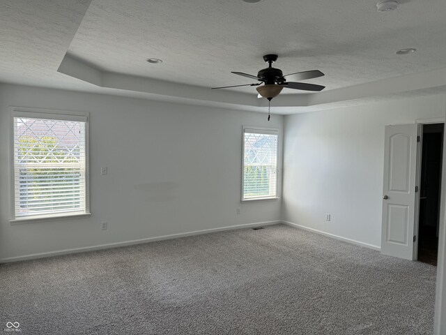 carpeted empty room with ceiling fan, a raised ceiling, and a textured ceiling