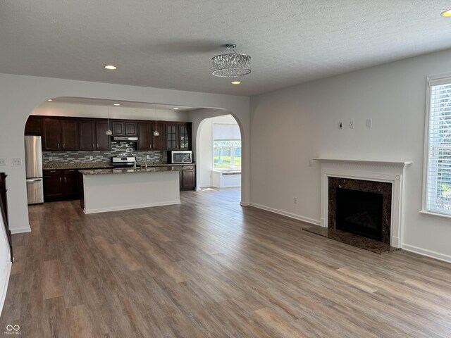 kitchen featuring dark brown cabinetry, tasteful backsplash, appliances with stainless steel finishes, dark hardwood / wood-style flooring, and a kitchen island with sink