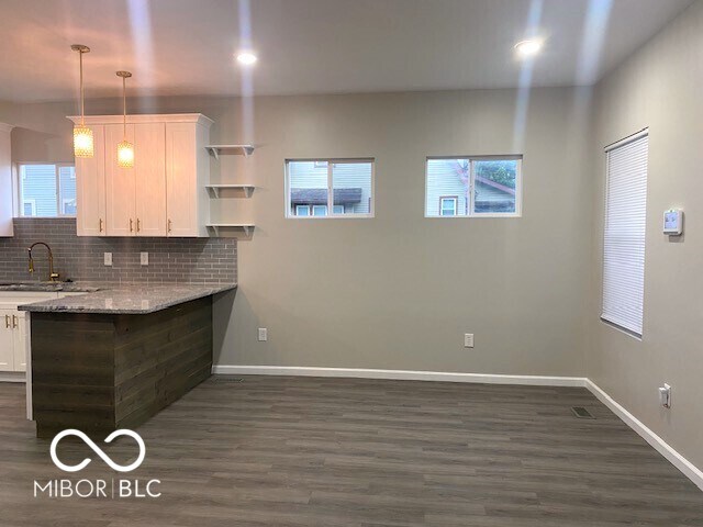 kitchen featuring decorative backsplash, white cabinetry, light stone countertops, and dark hardwood / wood-style flooring