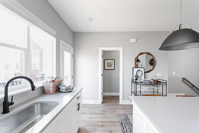 kitchen with sink, white cabinetry, light wood-type flooring, and pendant lighting