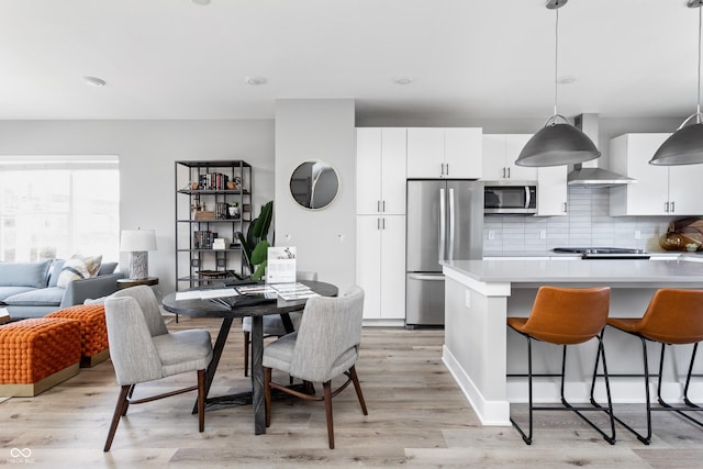 kitchen with white cabinets, stainless steel appliances, wall chimney exhaust hood, and decorative light fixtures