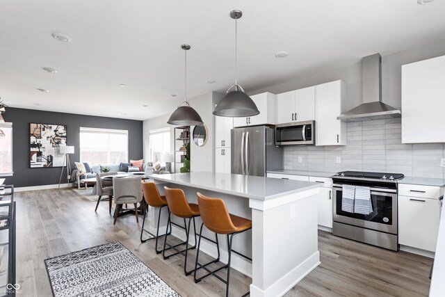 kitchen featuring tasteful backsplash, wall chimney range hood, white cabinets, a center island, and stainless steel appliances