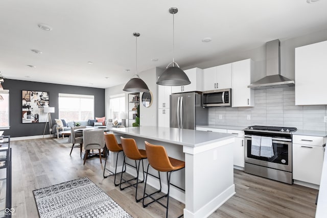 kitchen with white cabinetry, a kitchen island, wall chimney range hood, and stainless steel appliances