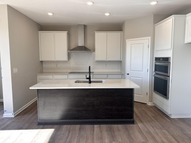 kitchen with a kitchen island with sink, white cabinets, wall chimney range hood, dark hardwood / wood-style flooring, and stainless steel double oven