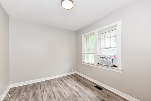 spare room with a textured ceiling, light hardwood / wood-style floors, and cooling unit