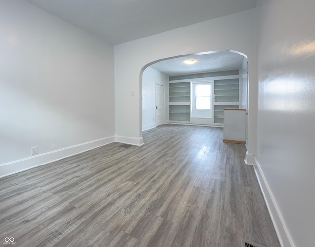 unfurnished room featuring built in features and hardwood / wood-style flooring