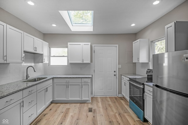 kitchen featuring a skylight, stainless steel appliances, light hardwood / wood-style flooring, and sink