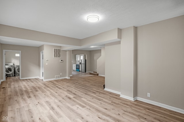 interior space with a textured ceiling, light wood-type flooring, and washing machine and clothes dryer