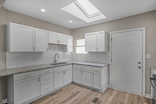 kitchen with a skylight, white cabinetry, tasteful backsplash, light wood-type flooring, and sink