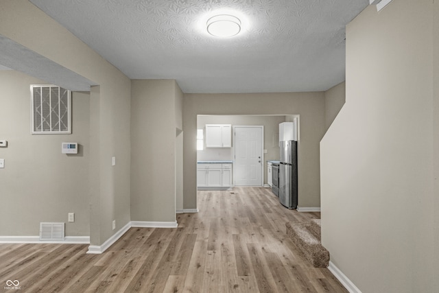 hallway with light wood-type flooring and a textured ceiling