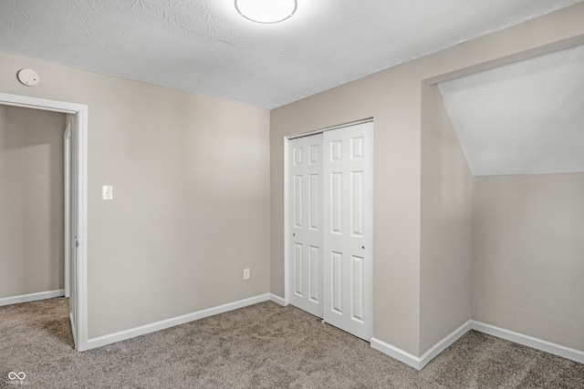 unfurnished bedroom with vaulted ceiling, carpet, a closet, and a textured ceiling