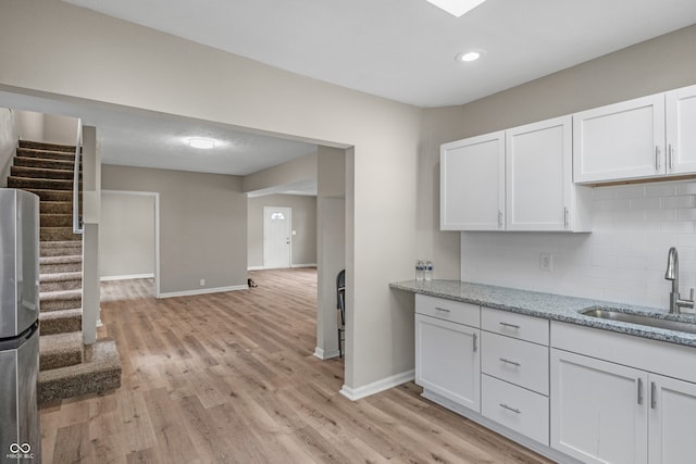 kitchen featuring sink, light hardwood / wood-style flooring, white cabinets, and tasteful backsplash