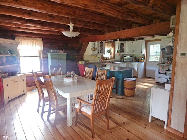 dining room with log walls, light wood-type flooring, and beam ceiling