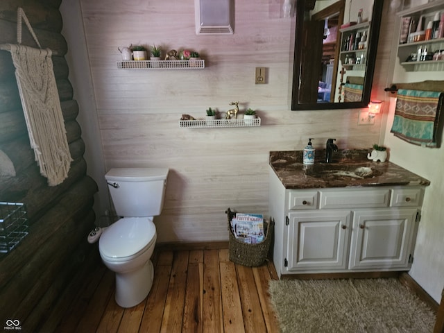 half bath featuring baseboards, vanity, toilet, and wood finished floors