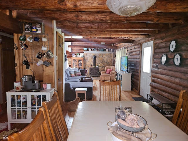 dining space featuring light wood finished floors, beamed ceiling, and a wood stove