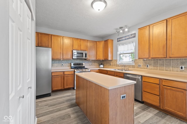 kitchen featuring stainless steel appliances, tasteful backsplash, light wood-type flooring, a kitchen island, and sink