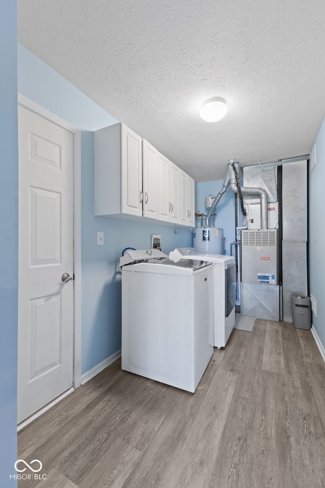 laundry area featuring washer and dryer, cabinets, a textured ceiling, and light hardwood / wood-style flooring