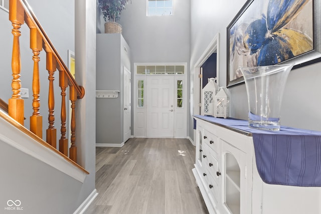 entryway with a healthy amount of sunlight, a towering ceiling, and light hardwood / wood-style flooring