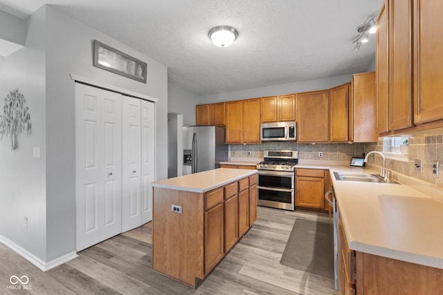 kitchen with a textured ceiling, a kitchen island, stainless steel appliances, light hardwood / wood-style floors, and sink