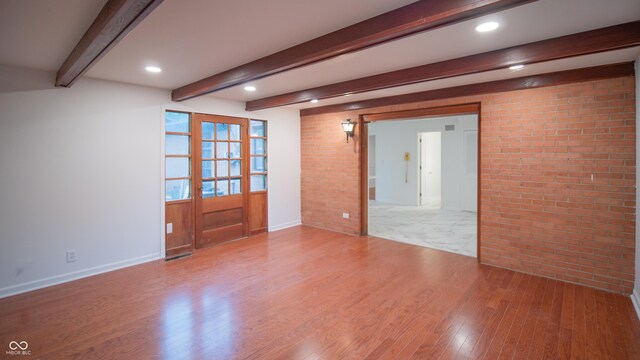 unfurnished room with beamed ceiling, brick wall, wood-type flooring, and french doors