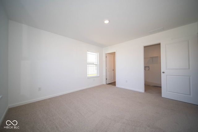 unfurnished bedroom with a walk in closet, light colored carpet, and a closet