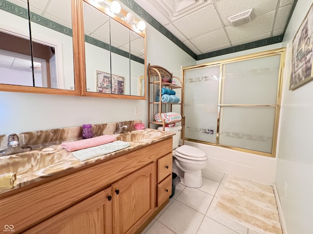 full bathroom featuring toilet, bath / shower combo with glass door, vanity, tile patterned flooring, and a drop ceiling