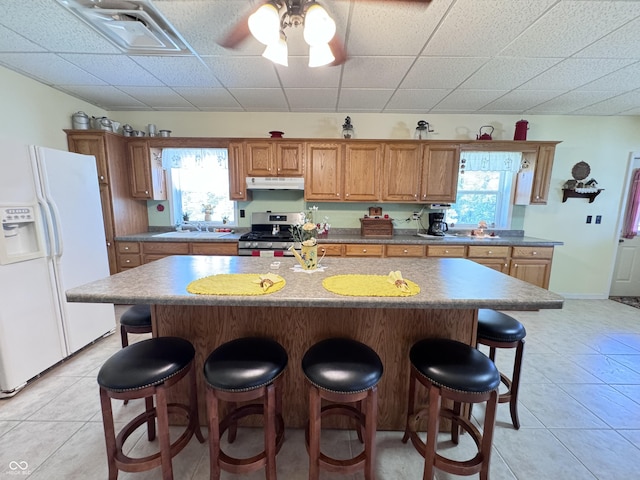 kitchen featuring a kitchen island, a breakfast bar, stainless steel gas range oven, and white fridge with ice dispenser