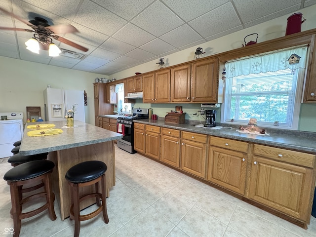 kitchen with a paneled ceiling, a breakfast bar, stainless steel range with gas stovetop, white refrigerator with ice dispenser, and a kitchen island