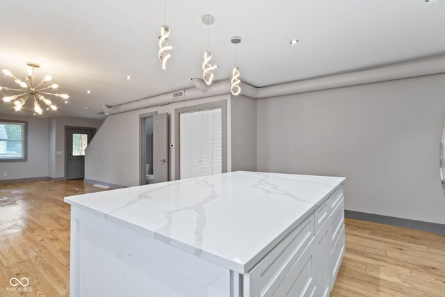 kitchen with light wood-type flooring, white cabinets, a center island, a notable chandelier, and hanging light fixtures