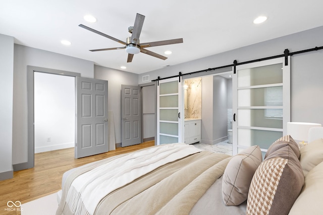 bedroom with ceiling fan, connected bathroom, light hardwood / wood-style flooring, and a barn door