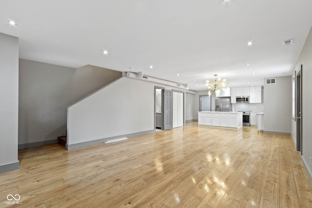 unfurnished living room featuring a notable chandelier, light hardwood / wood-style floors, and a barn door