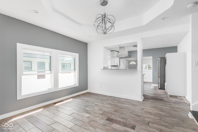 unfurnished living room featuring an inviting chandelier, hardwood / wood-style flooring, and a tray ceiling