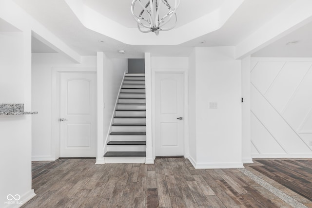 stairway featuring hardwood / wood-style flooring, a raised ceiling, and a chandelier