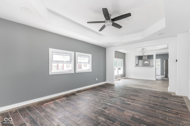 unfurnished living room featuring ceiling fan, dark hardwood / wood-style floors, a wealth of natural light, and a tray ceiling