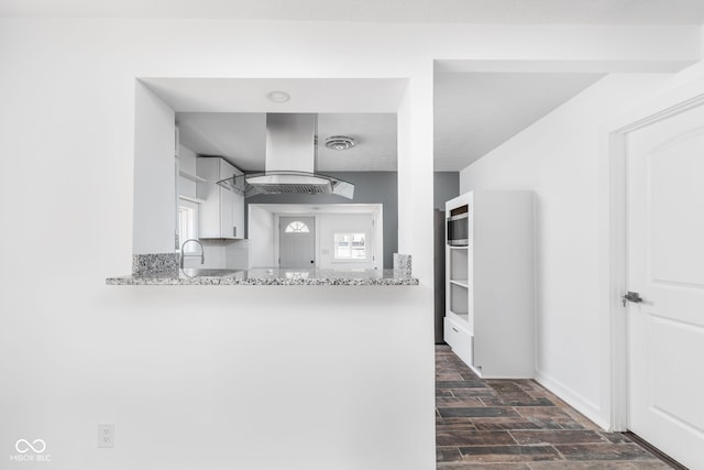 kitchen with white cabinetry, light stone countertops, island range hood, and sink