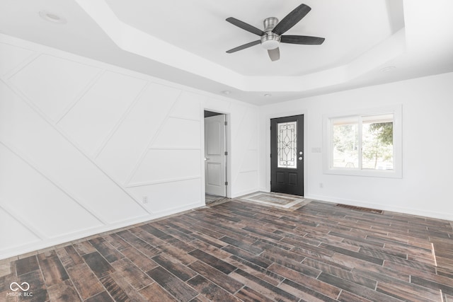 foyer entrance with wood-type flooring, ceiling fan, and a raised ceiling