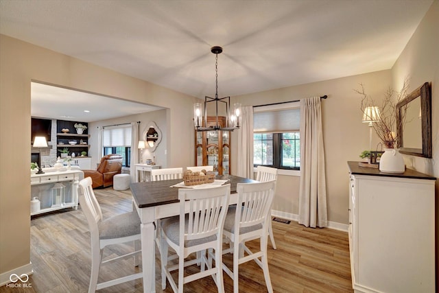 dining room featuring a stone fireplace, light hardwood / wood-style floors, and a chandelier