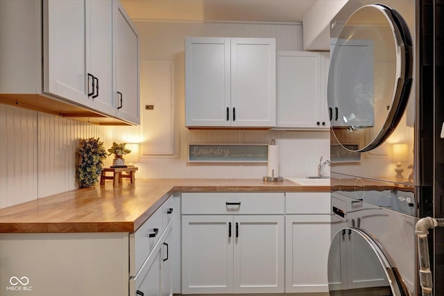 kitchen with white cabinetry, stacked washer / drying machine, wood counters, and sink