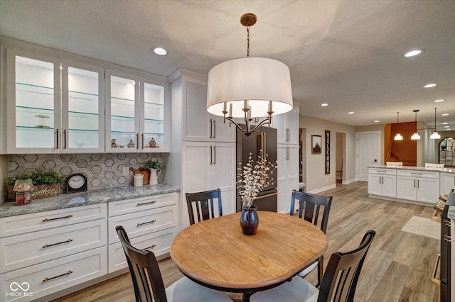 dining area featuring light wood-type flooring, a textured ceiling, and an inviting chandelier