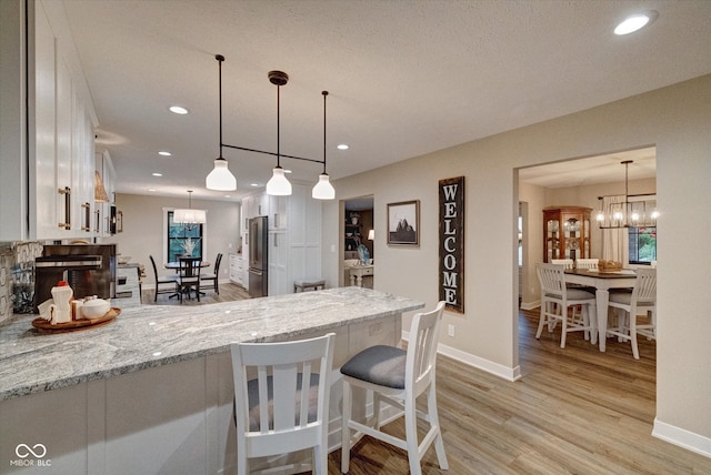 kitchen featuring hanging light fixtures, white cabinetry, light hardwood / wood-style flooring, and light stone countertops