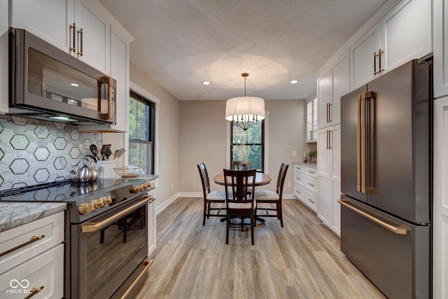 kitchen featuring backsplash, white cabinets, premium appliances, and light hardwood / wood-style flooring