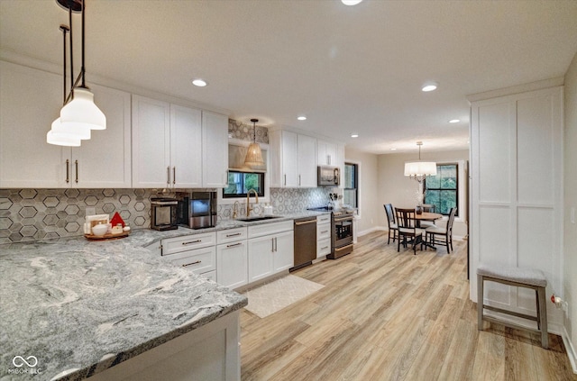 kitchen with sink, appliances with stainless steel finishes, pendant lighting, light stone countertops, and white cabinets