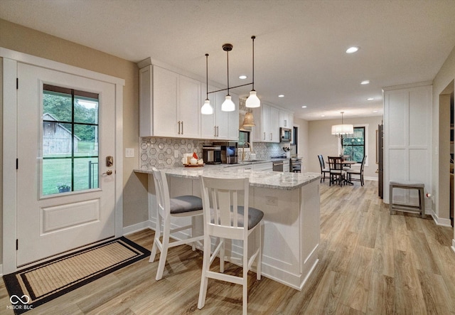 kitchen with kitchen peninsula, pendant lighting, light stone countertops, decorative backsplash, and white cabinets