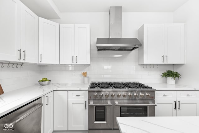 kitchen with decorative backsplash, appliances with stainless steel finishes, wall chimney range hood, and white cabinetry