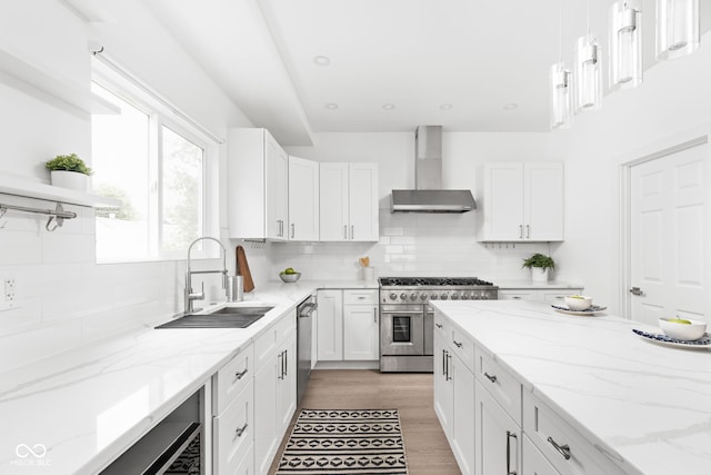 kitchen with stainless steel appliances, light hardwood / wood-style floors, sink, decorative backsplash, and wall chimney range hood